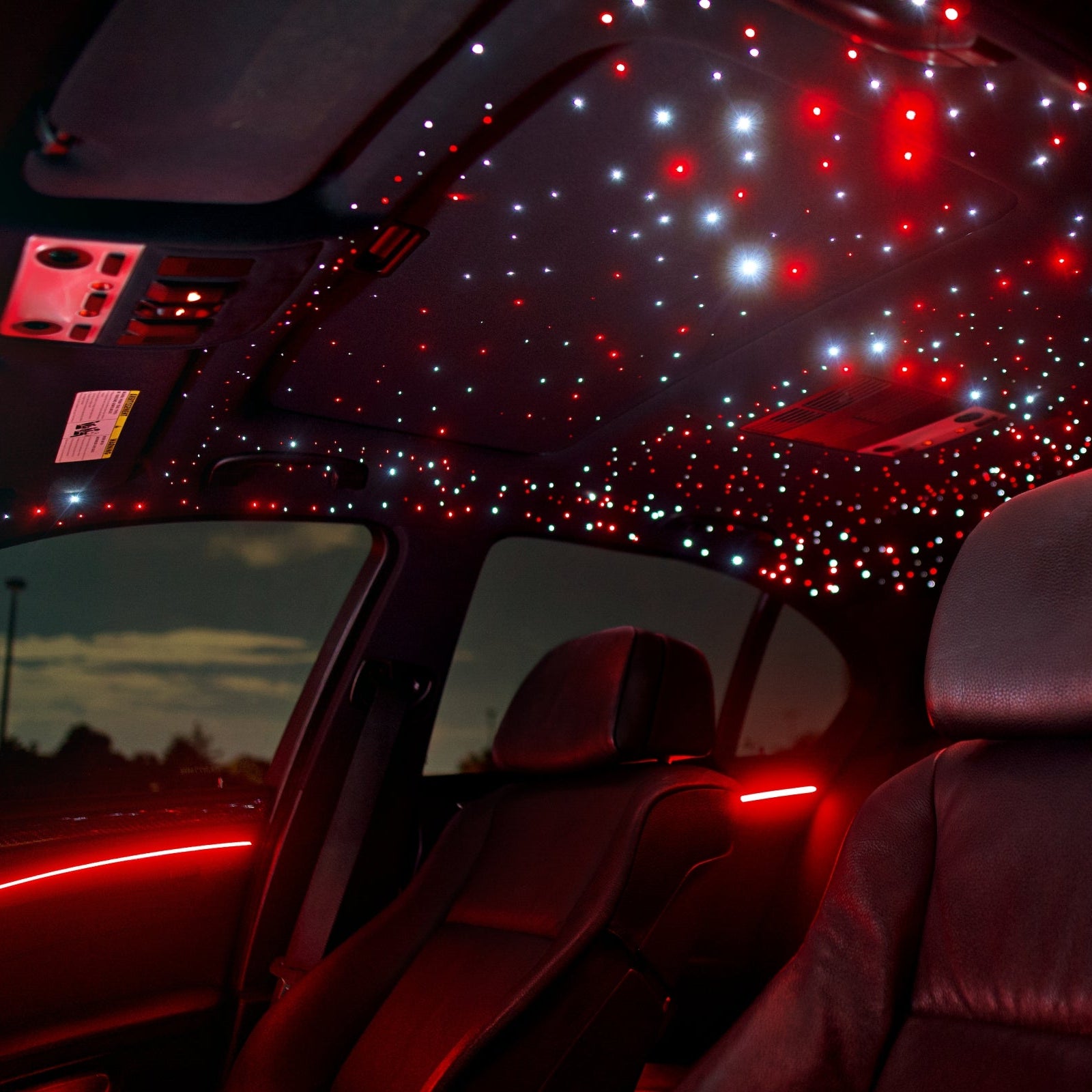 Custom BMW interior featuring mixed red and white starlight headliner kit with matching red ambient door lighting viewed from the rear seat