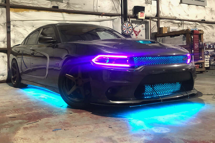 Custom Dodge Charger SRT featuring cyan blue underglow kit and contrasting pink demon eye headlights, installed in a performance shop
