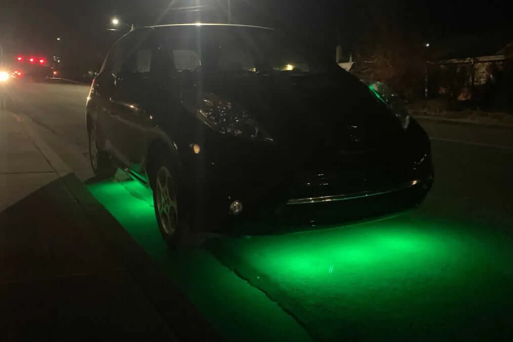 "Custom green LED underglow lighting kit installed on black Nissan Leaf EV parked on a residential street at night