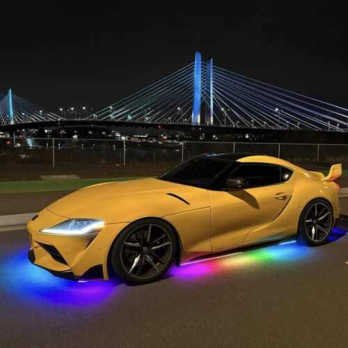 Yellow sports car with RGB underglow lighting in front of a bridge at night
