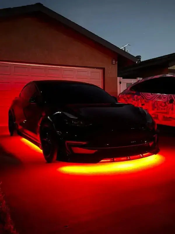 Custom bright red LED underglow lighting kit installed on black Tesla Model 3 parked in a driveway at night