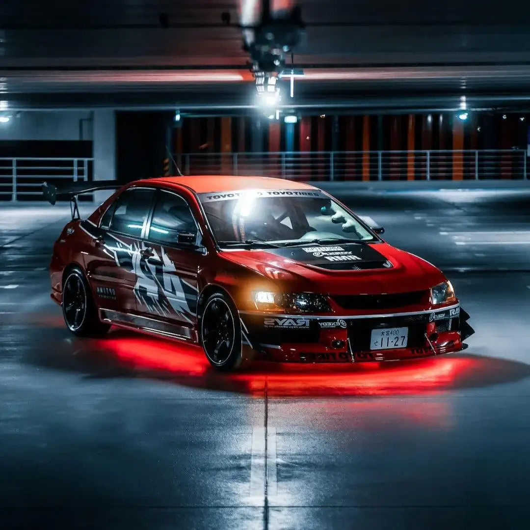 Red sports car with custom modifications in a dark parking lot setting with underbody lights/ underglow