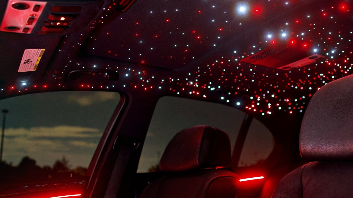 Car interior with a red and white starlight headliner glowing across the roof, viewed from the rear seat