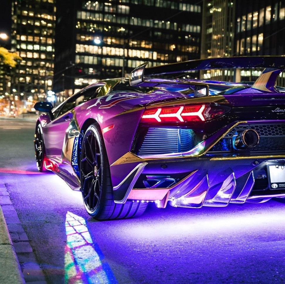 lamborghini sports car with vibrant purple and gold design on a city street at night. displaying underbody lights/underglow