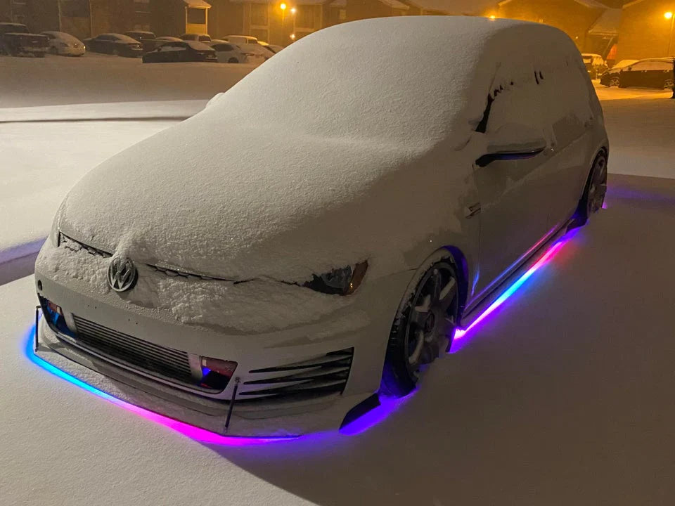 White VW covered in snow with RGB underglow lights on a snowy street.
