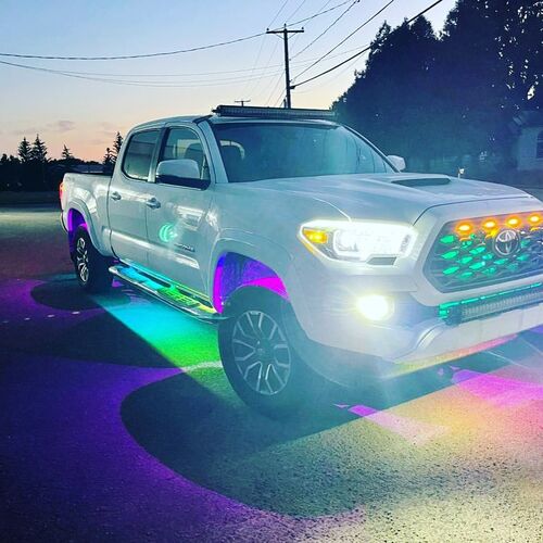 White toyota pickup truck with colorful LED lights on a road at dusk with under-body RGB lights/underglow fast and furious lights 